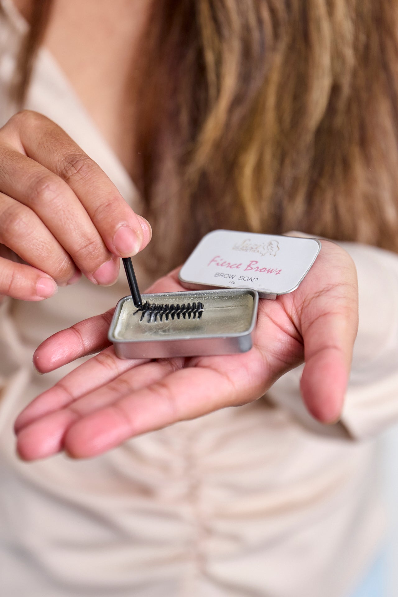 A woman holding a compact container of Suzi Kozmetika brow soap in her hand.