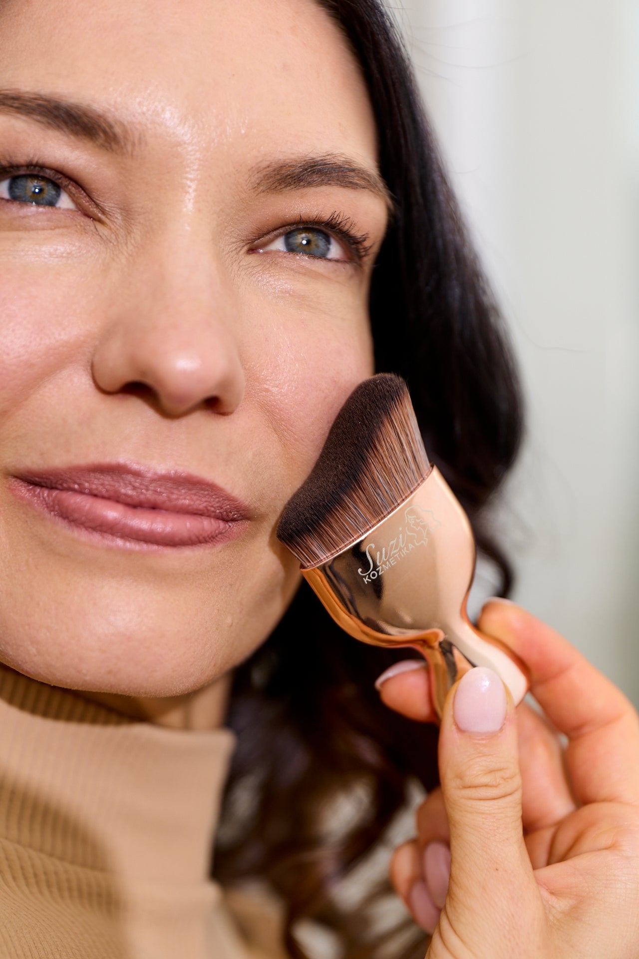 A woman applying makeup with the Luxe Buffer Brush from Suzi Kozmetika, achieving flawless and professional results.